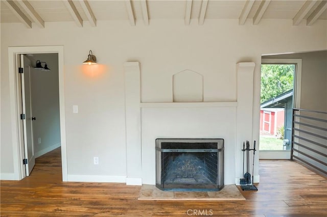 unfurnished living room featuring beam ceiling, wood finished floors, a healthy amount of sunlight, and a fireplace with raised hearth