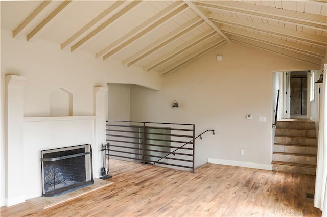 unfurnished living room with a fireplace with raised hearth, lofted ceiling with beams, baseboards, and wood finished floors