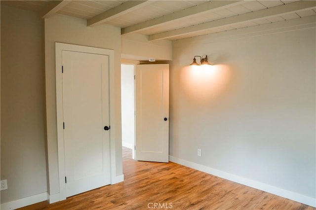 spare room with baseboards, beam ceiling, wood finished floors, and wooden ceiling