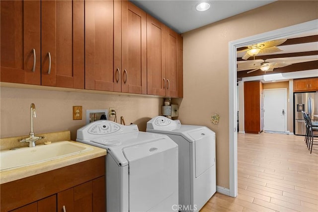 clothes washing area featuring light wood-style flooring, cabinet space, independent washer and dryer, a ceiling fan, and a sink