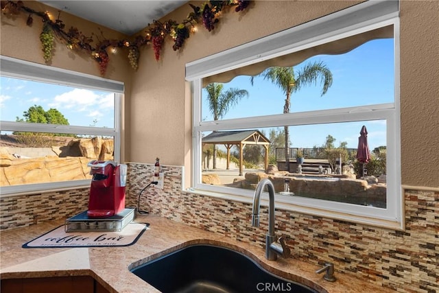 kitchen with decorative backsplash, light stone countertops, a textured wall, and a sink