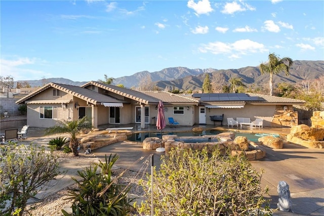 view of front of house featuring stucco siding, solar panels, a mountain view, and a patio area