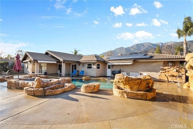 rear view of house with a patio, a tiled roof, roof mounted solar panels, and stucco siding