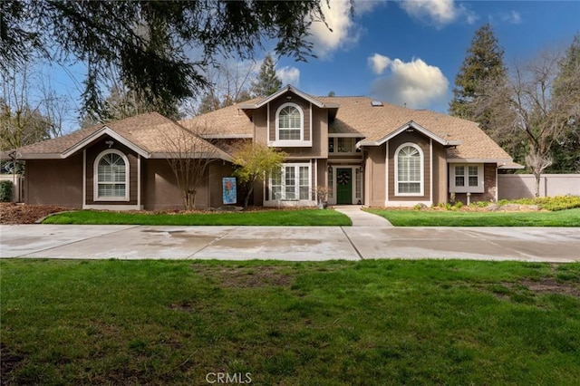 traditional home with driveway, stucco siding, and a front yard