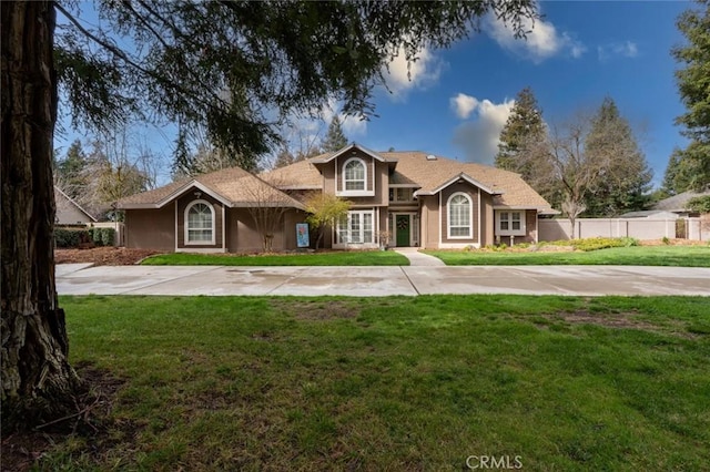 traditional home featuring driveway, fence, a front lawn, and stucco siding