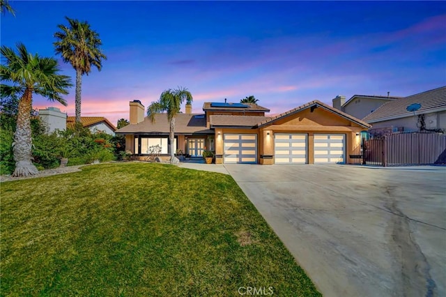 view of front of property featuring an attached garage, solar panels, a yard, concrete driveway, and a gate