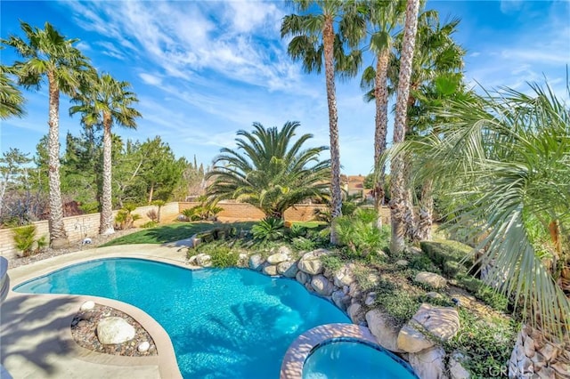 view of swimming pool featuring a pool with connected hot tub and fence