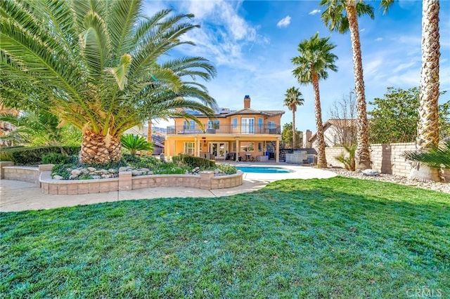 rear view of property featuring a yard, a patio area, fence, a balcony, and an outdoor pool