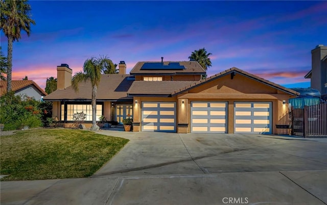 view of front of property with a garage, a yard, concrete driveway, a tiled roof, and roof mounted solar panels