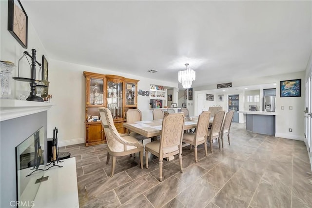 dining space featuring baseboards, a fireplace, and an inviting chandelier