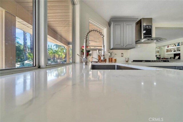 kitchen with stainless steel cooktop, wall chimney range hood, a sink, and gray cabinetry