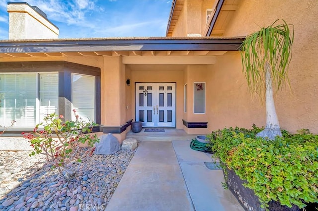 property entrance with a chimney, french doors, and stucco siding