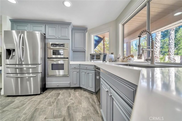 kitchen featuring light countertops, stainless steel appliances, gray cabinetry, a sink, and recessed lighting