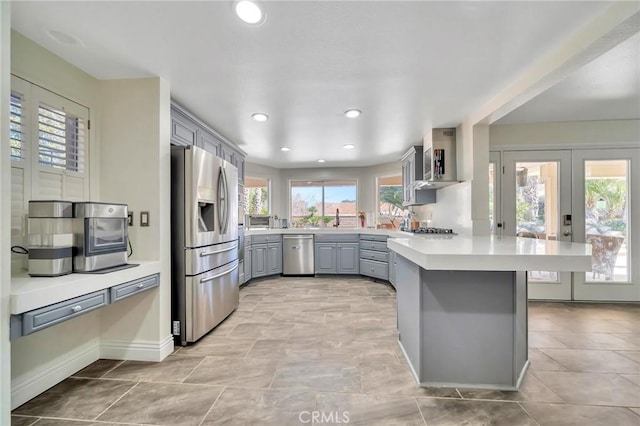 kitchen with a peninsula, plenty of natural light, appliances with stainless steel finishes, and gray cabinets