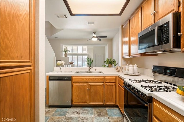 kitchen featuring brown cabinets, visible vents, appliances with stainless steel finishes, a sink, and a peninsula