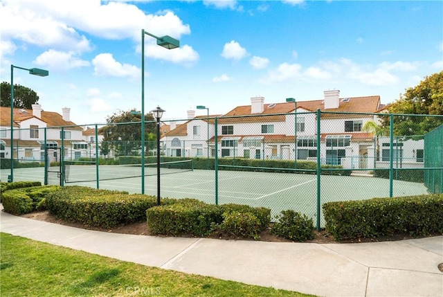 view of tennis court with fence and a residential view