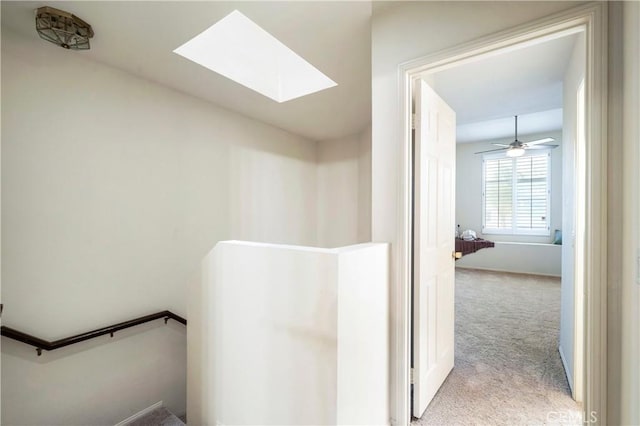 hall with light carpet, a skylight, and an upstairs landing