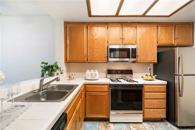 kitchen with tile countertops, appliances with stainless steel finishes, brown cabinetry, and a sink