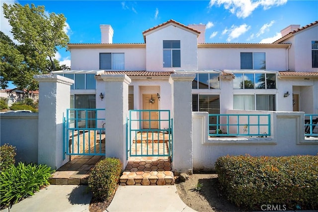 exterior space with a tile roof, a chimney, stucco siding, a gate, and fence