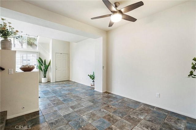 unfurnished room with a ceiling fan, stone finish floor, and baseboards