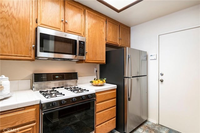 kitchen with appliances with stainless steel finishes, brown cabinetry, and tile counters