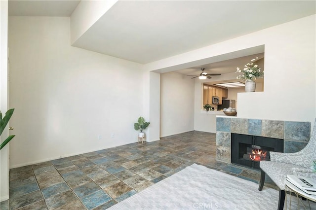 living area featuring baseboards, stone finish floor, a ceiling fan, and a tile fireplace