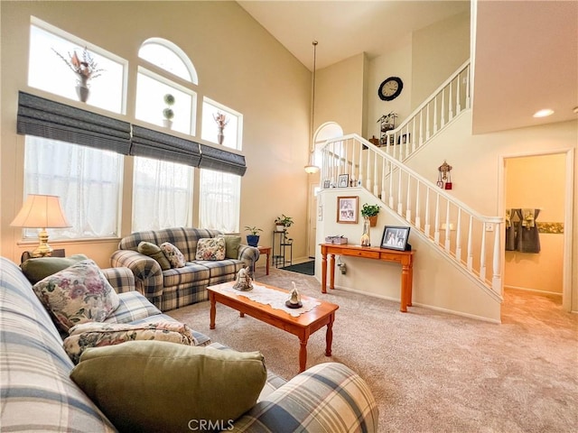 living area featuring stairway, carpet floors, baseboards, and a towering ceiling