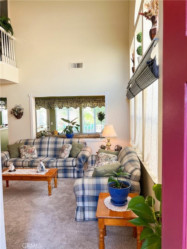 carpeted living area with a high ceiling and visible vents