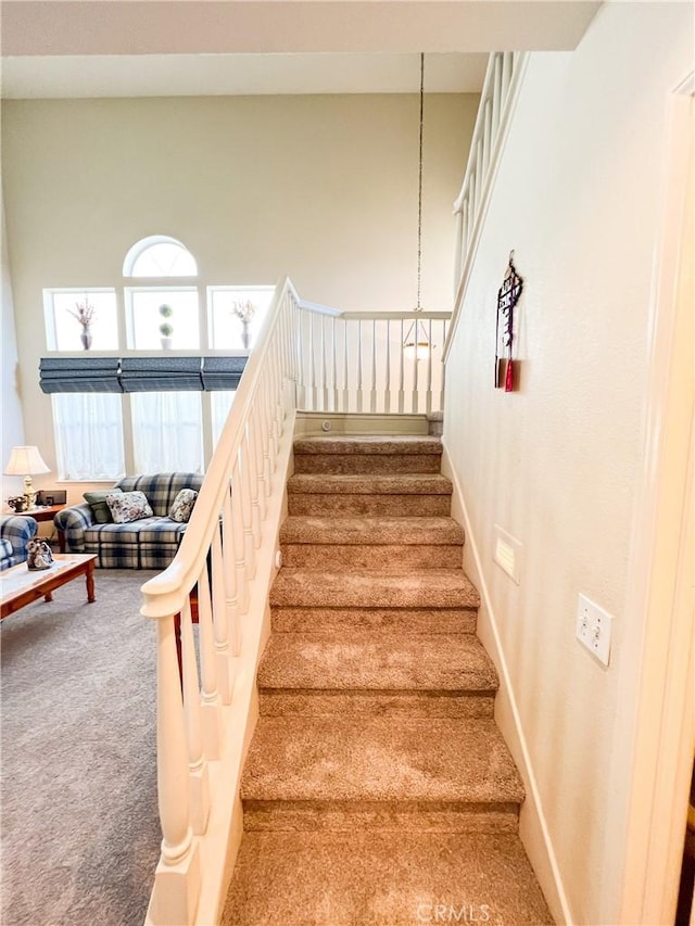 staircase with a towering ceiling, baseboards, and carpet floors