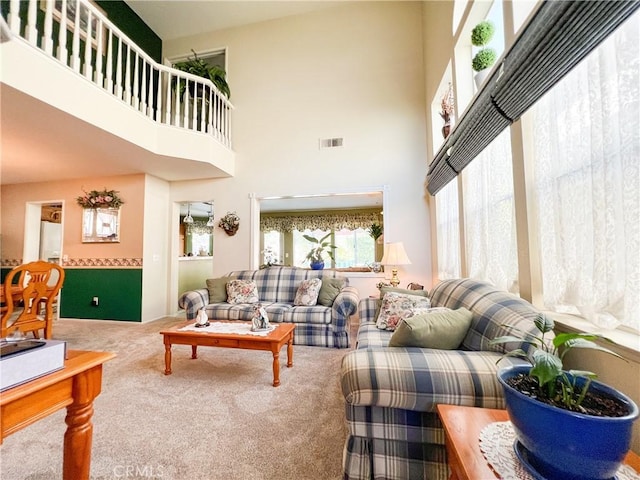 living room with a towering ceiling, visible vents, and carpet floors