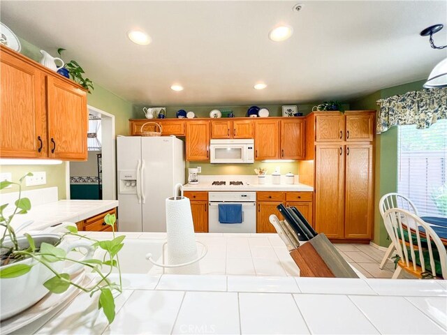 kitchen with tile counters, light tile patterned floors, recessed lighting, brown cabinets, and white appliances