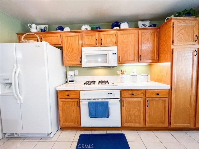 kitchen with light tile patterned floors, white appliances, tile counters, and brown cabinetry