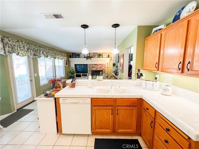 kitchen featuring light tile patterned floors, a peninsula, a fireplace, white dishwasher, and a sink