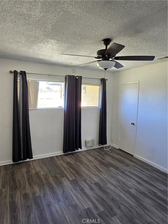 empty room with a textured ceiling, wood finished floors, visible vents, and baseboards