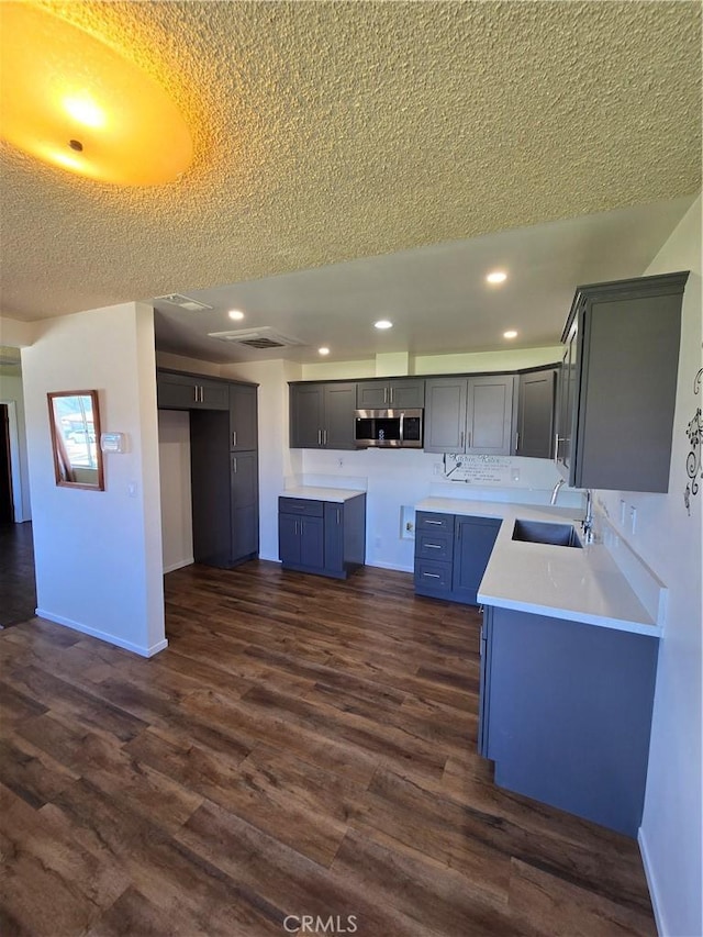 kitchen featuring dark wood finished floors, recessed lighting, stainless steel microwave, a sink, and a textured ceiling