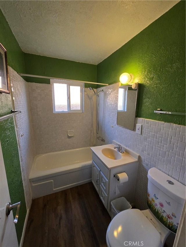 full bathroom with a textured ceiling, a textured wall, toilet, wood finished floors, and shower / washtub combination