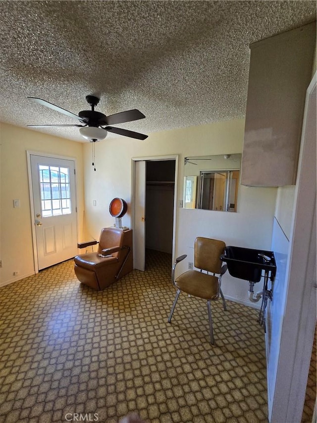 living area featuring ceiling fan, a textured ceiling, and baseboards