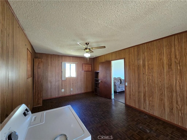 clothes washing area with a textured ceiling, wooden walls, a ceiling fan, baseboards, and washer / clothes dryer