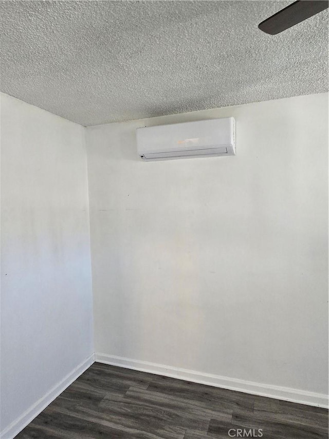 spare room with dark wood-style flooring, a wall unit AC, a textured ceiling, and baseboards