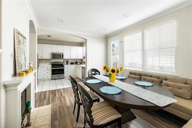 dining area with arched walkways, recessed lighting, light wood-style flooring, and crown molding