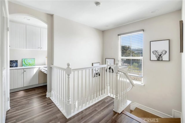 hall with dark wood-style floors, an upstairs landing, and baseboards