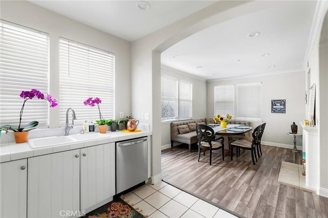 kitchen featuring arched walkways, tile countertops, light wood-type flooring, stainless steel dishwasher, and a sink