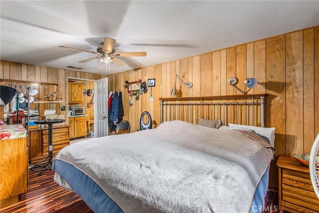 bedroom featuring dark wood-style floors, wood walls, a textured ceiling, and visible vents