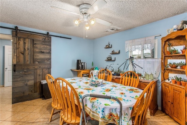 dining area with light tile patterned floors, a barn door, visible vents, ceiling fan, and a textured ceiling