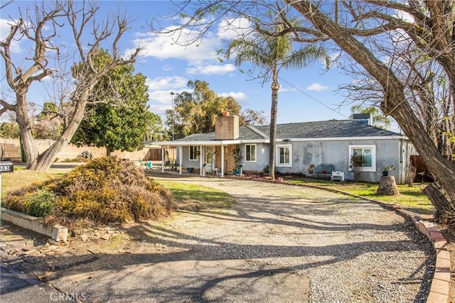 ranch-style home featuring driveway, a chimney, fence, and stucco siding