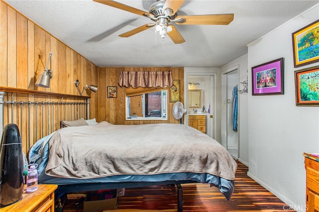 bedroom featuring a textured ceiling, ensuite bathroom, wooden walls, wood finished floors, and baseboards