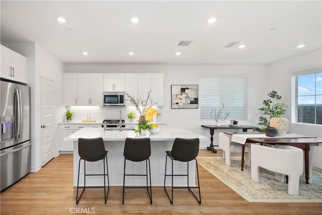 kitchen with a breakfast bar area, visible vents, a center island with sink, light countertops, and appliances with stainless steel finishes