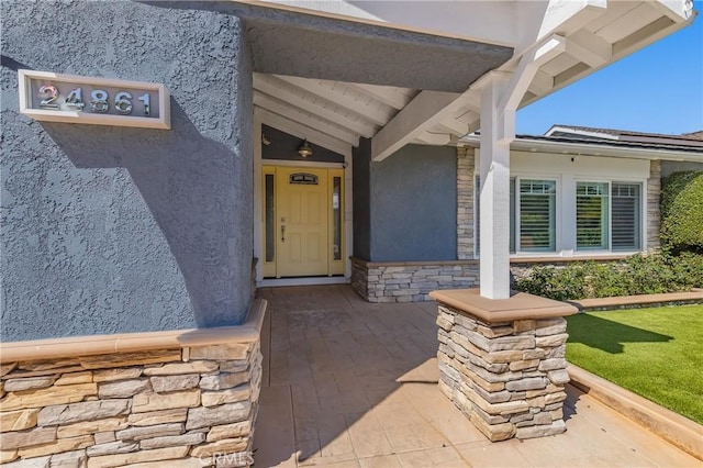 view of exterior entry featuring stone siding and stucco siding