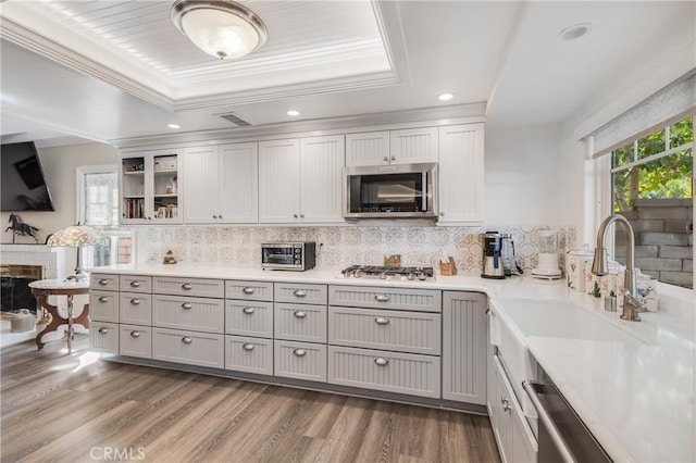 kitchen with appliances with stainless steel finishes, a raised ceiling, backsplash, and light wood finished floors