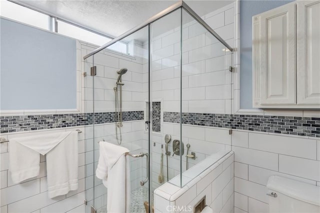 full bathroom featuring a shower stall, tile walls, toilet, and a textured ceiling